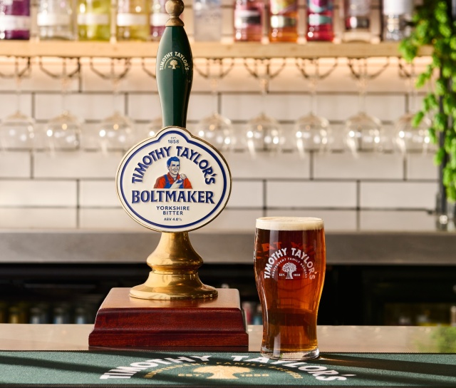 A pint of Timothy Taylor’s Boltmaker beside its beer pump on a pub bar.